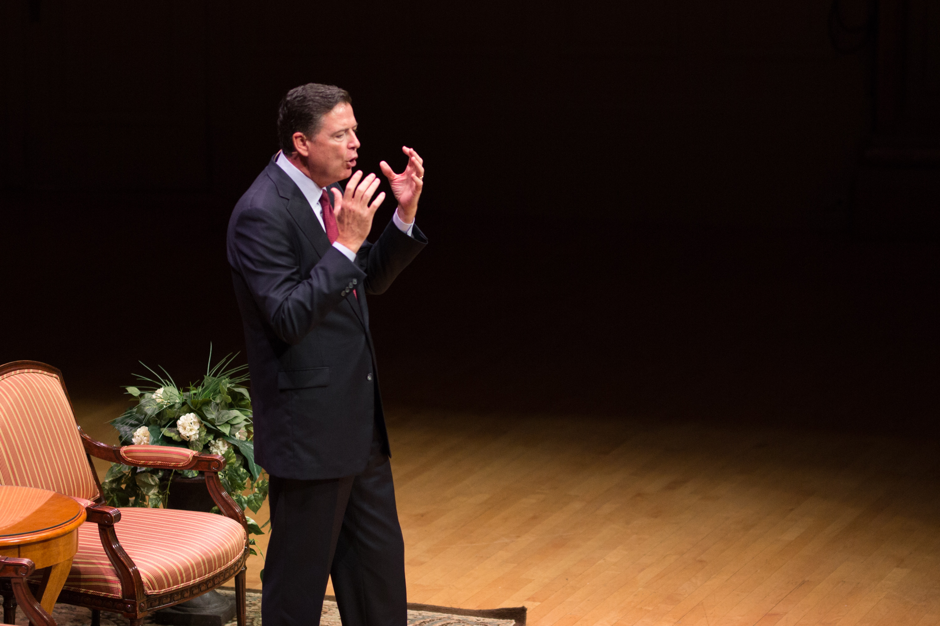 James Comey gestures with both hands while speaking on the Symphony Hall stage