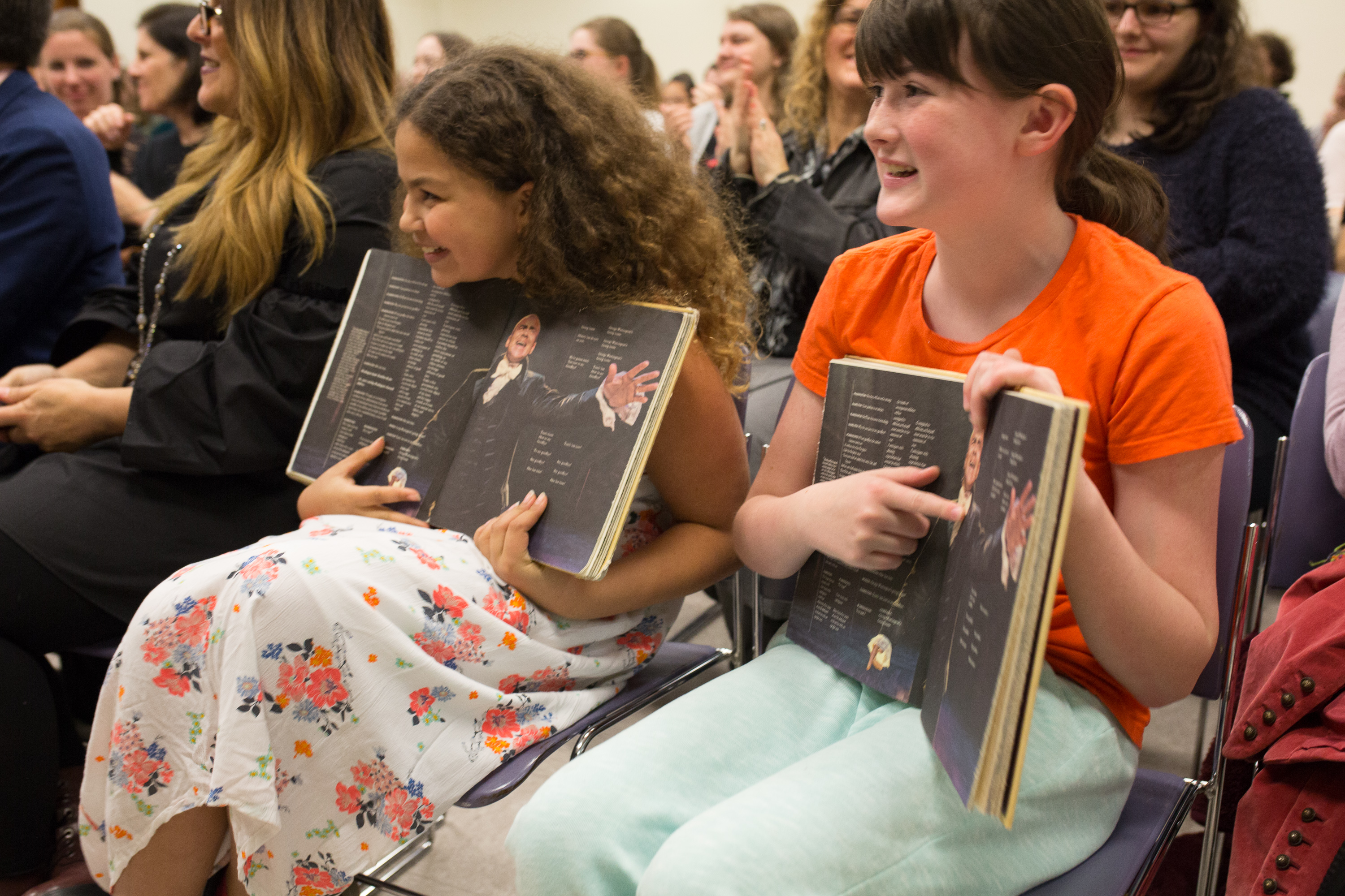 Two young girls hold open a page of the "Hamilton" book with Christopher Jackson's picture.
