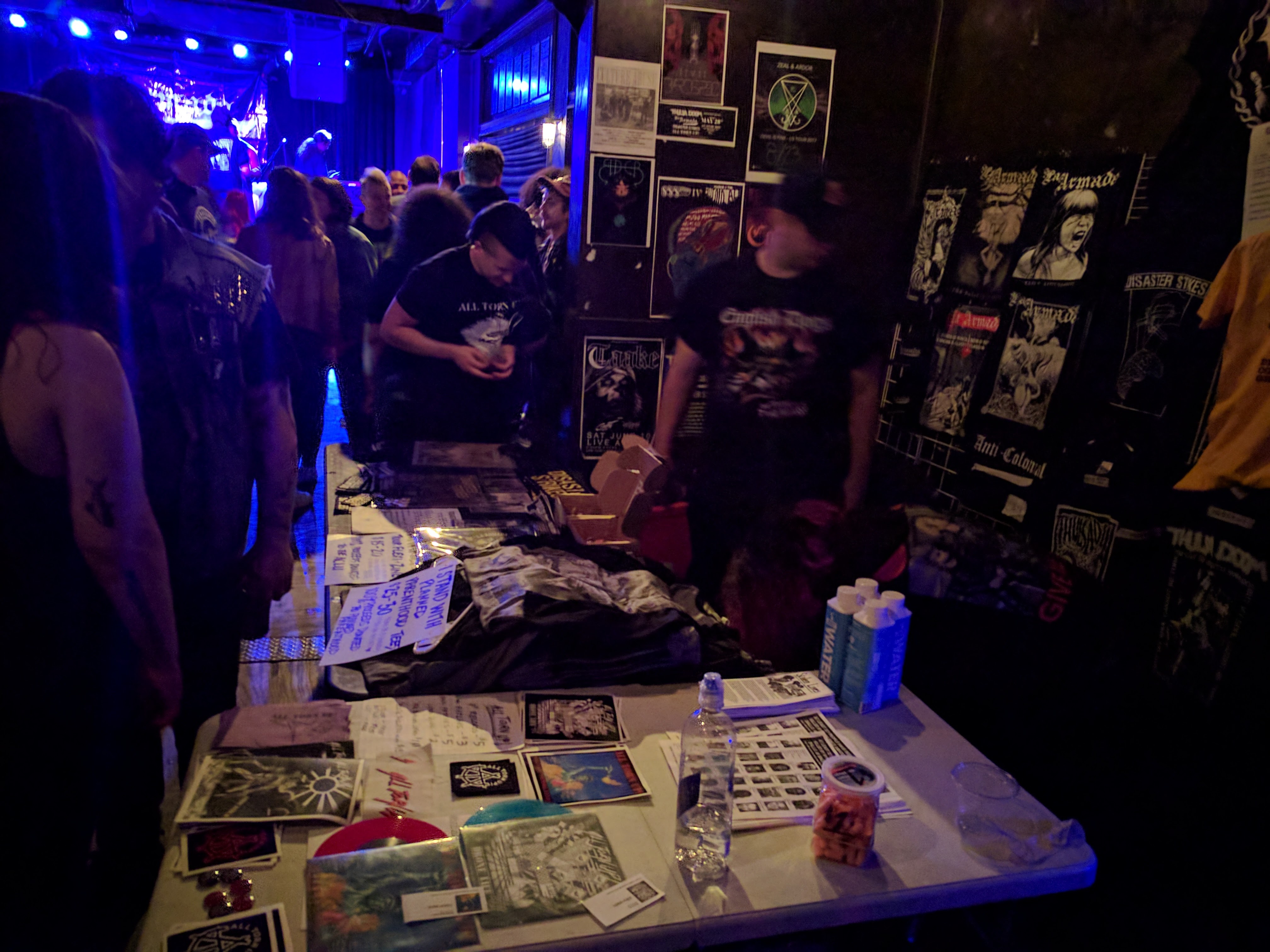 A scene from the tour with the merchandise table in the forefront and blue lights from the concert in the back.