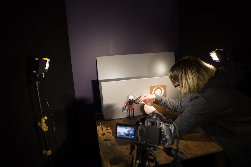 Woman manipulating small robot figure in front of a camera set-up on a tripod