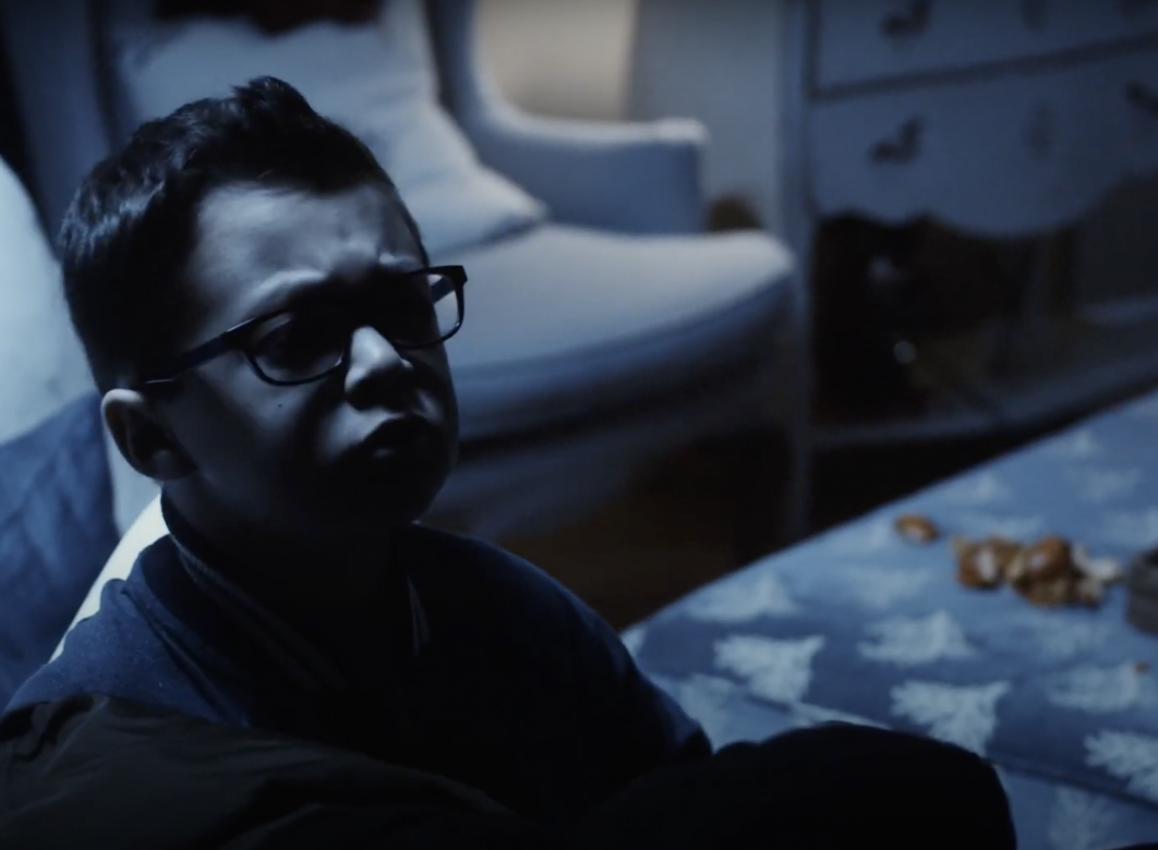 Small boy with glasses in a moonlit room looks worriedly off camera.