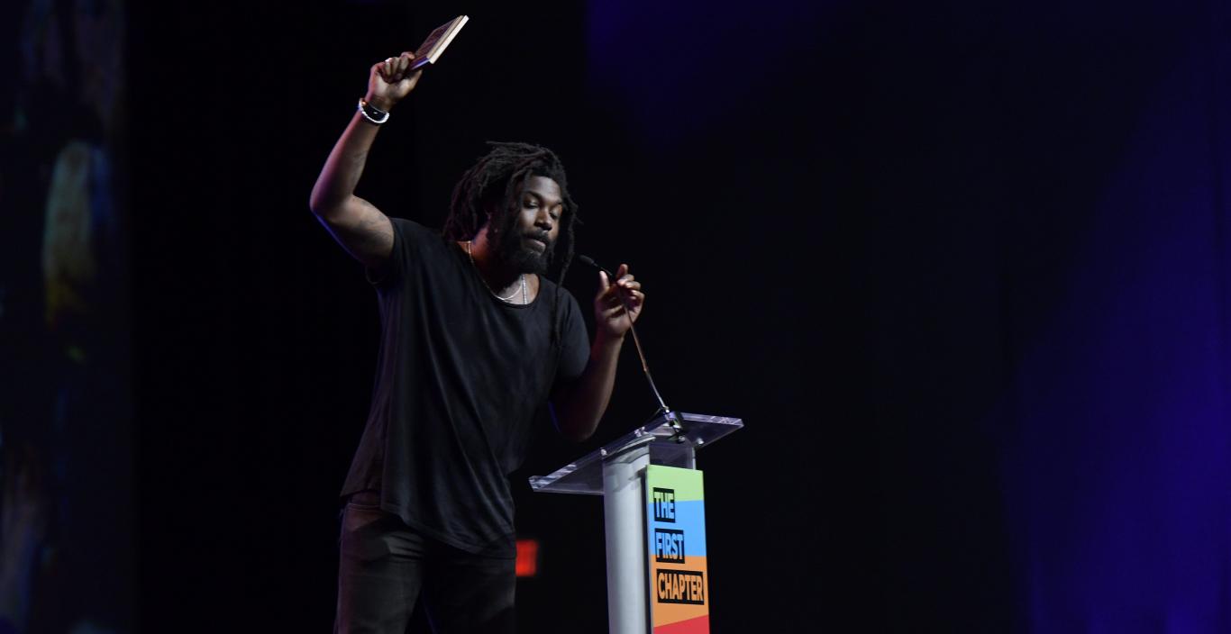 Author and creative writing faculty Jason Reynolds holds a book in the air as he speaks at the conference.