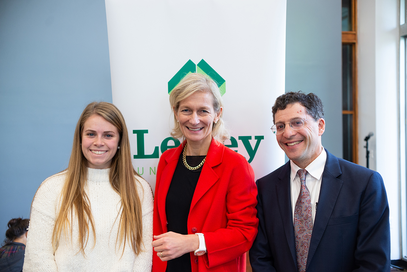 Two women and a man smiling and posing for a photo inside in front of a Lesley banner