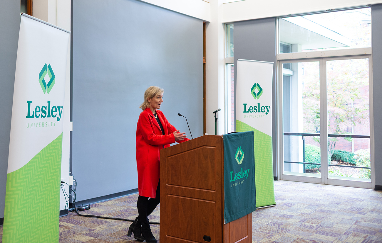 Woman in a red jacket standing at a podium in Lesley's Washburn Hall