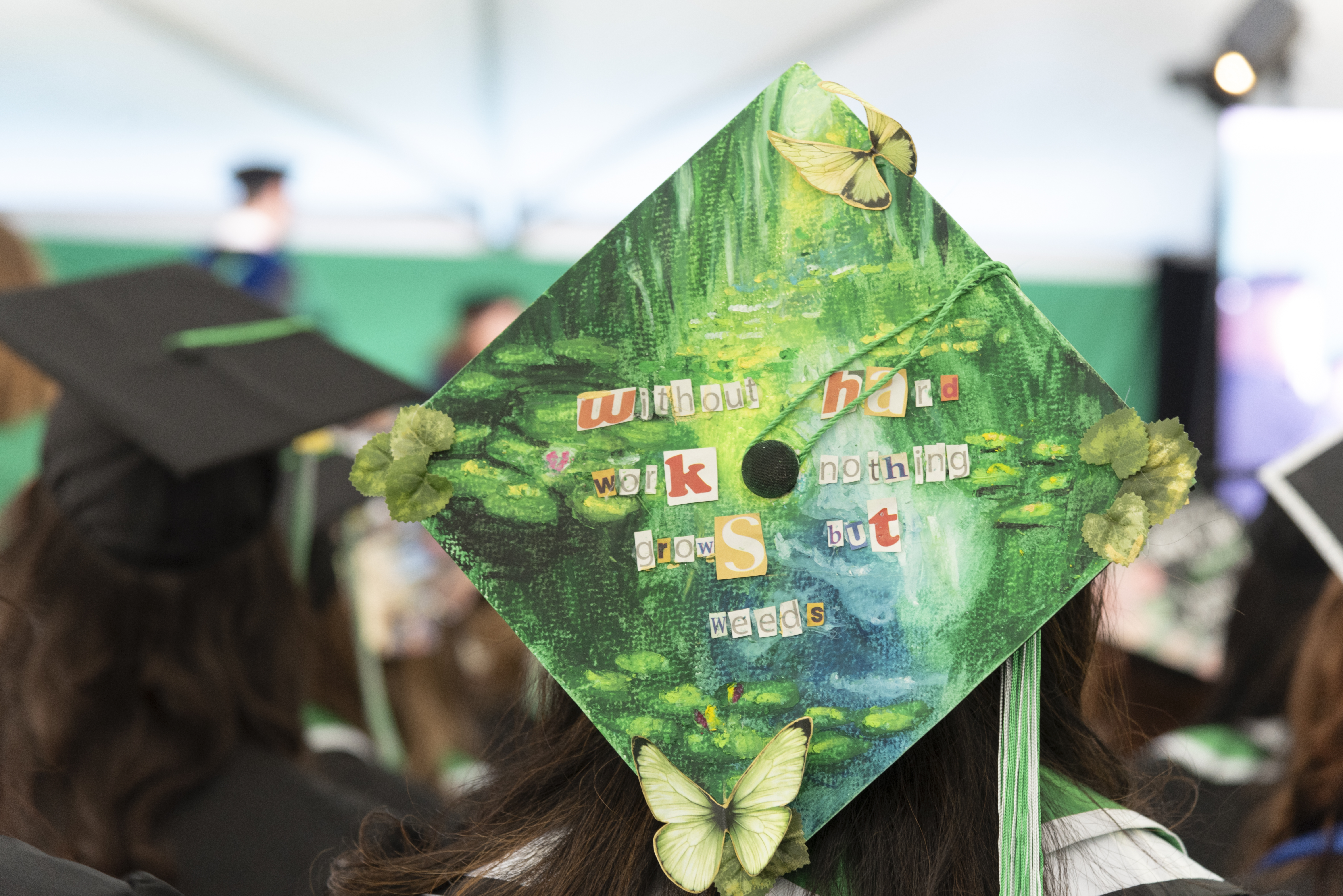 A graduate's cap, painted green with faux butterflies, with the words "Without hard work, nothing grows but weeds."