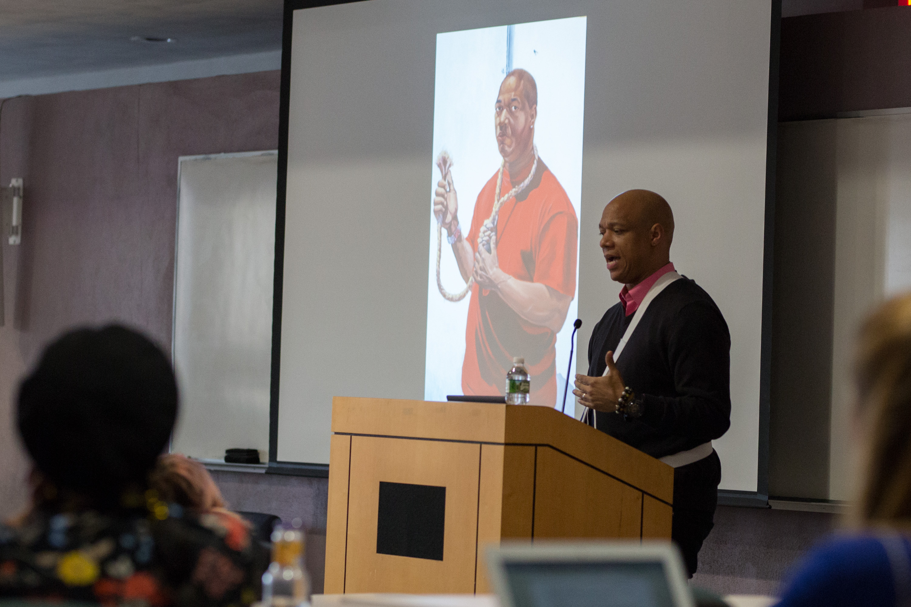 Joel Christian Gill is pictured at a podium with a photo slide of one of his paintings in the background