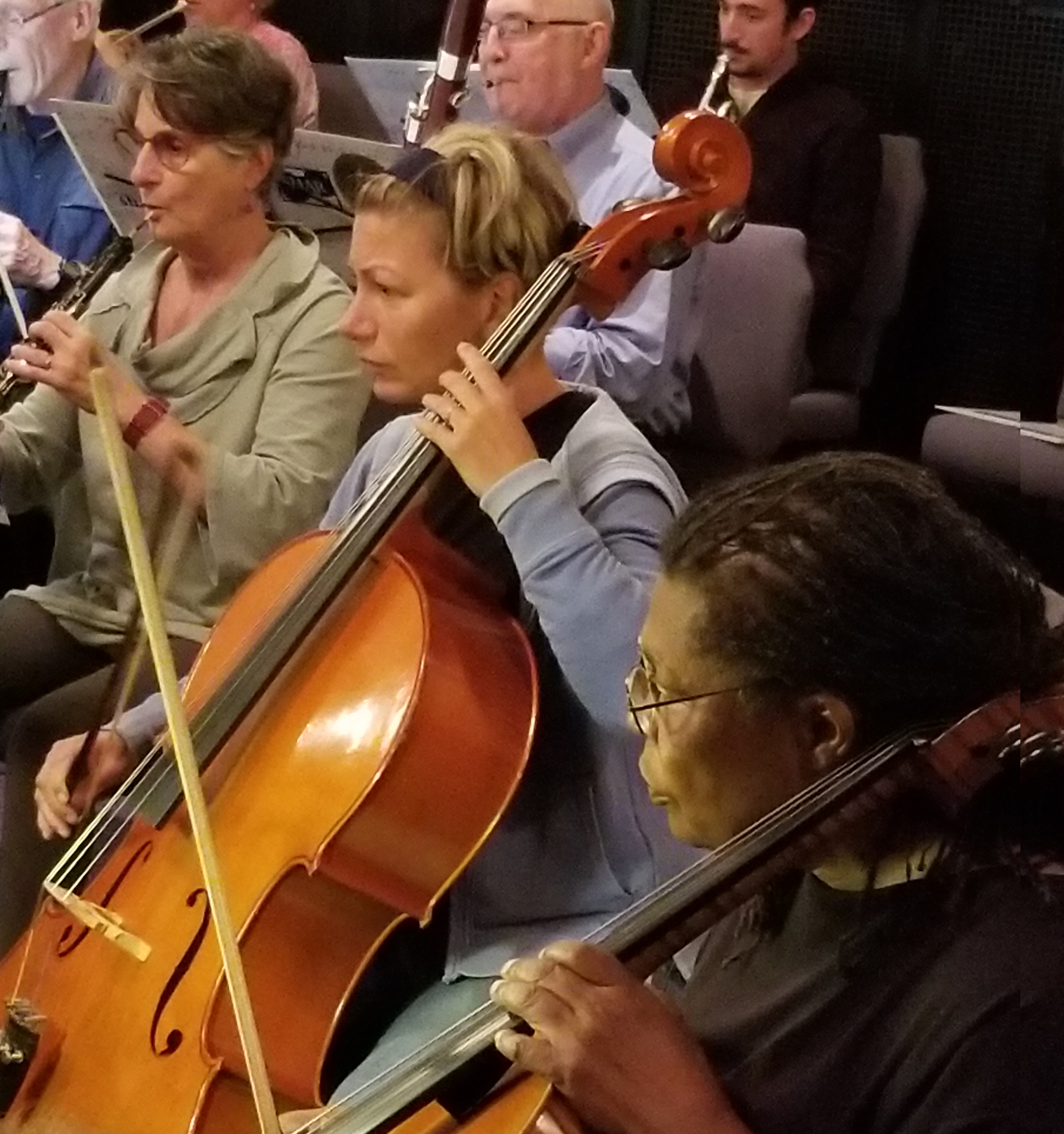 Woman seated and playing a cello in an orchestra.
