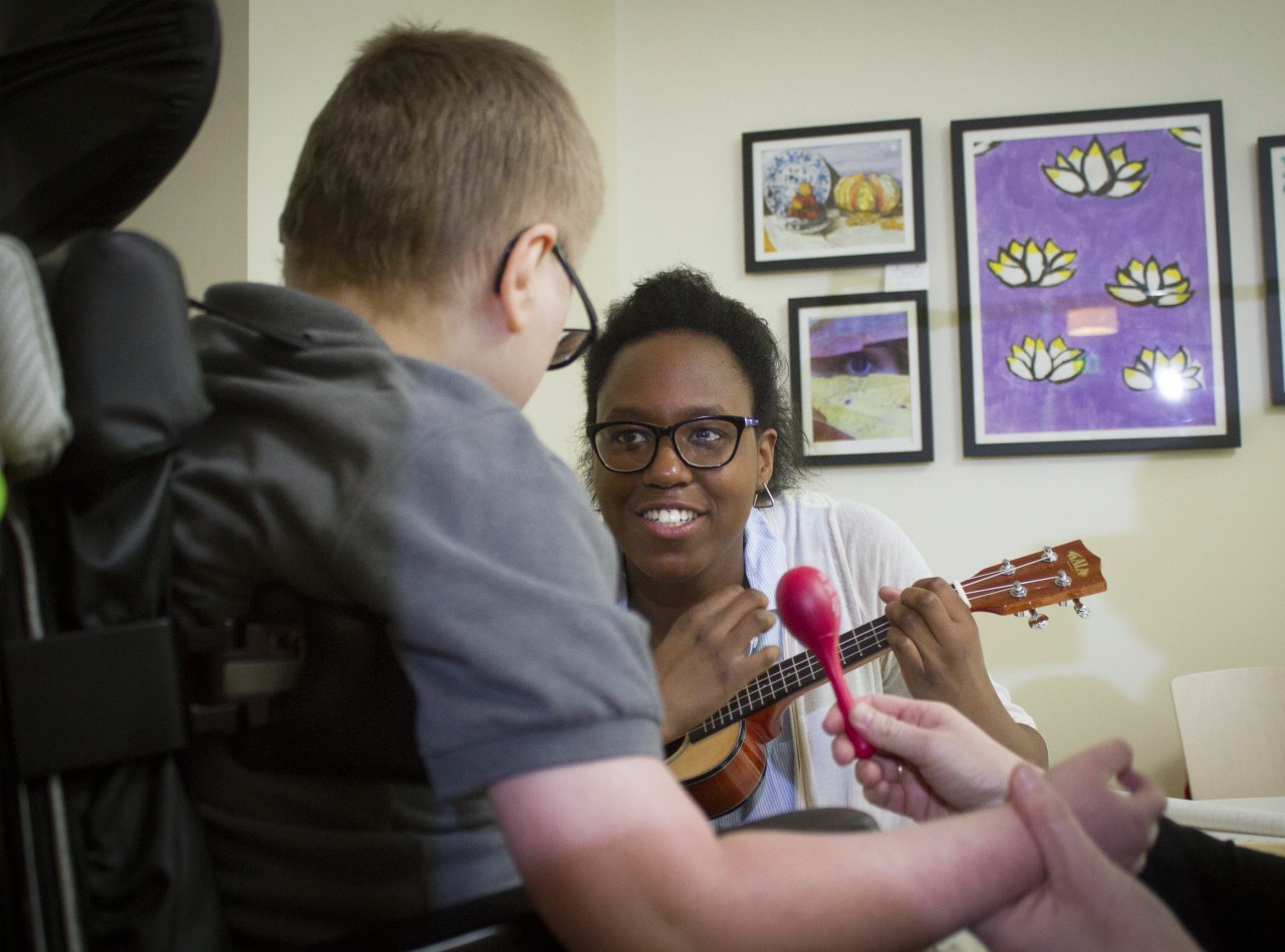 Woman plays ukulele for a child in a wheelchair