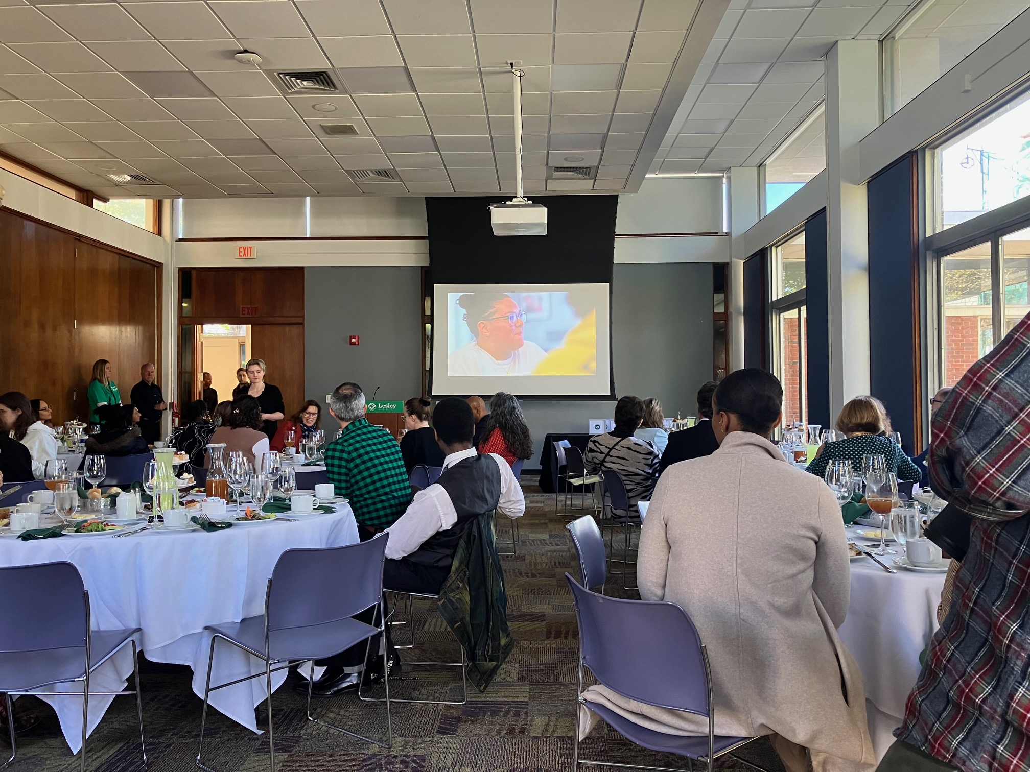 Washburn Lounge, people dinding at tables while video shown on screen