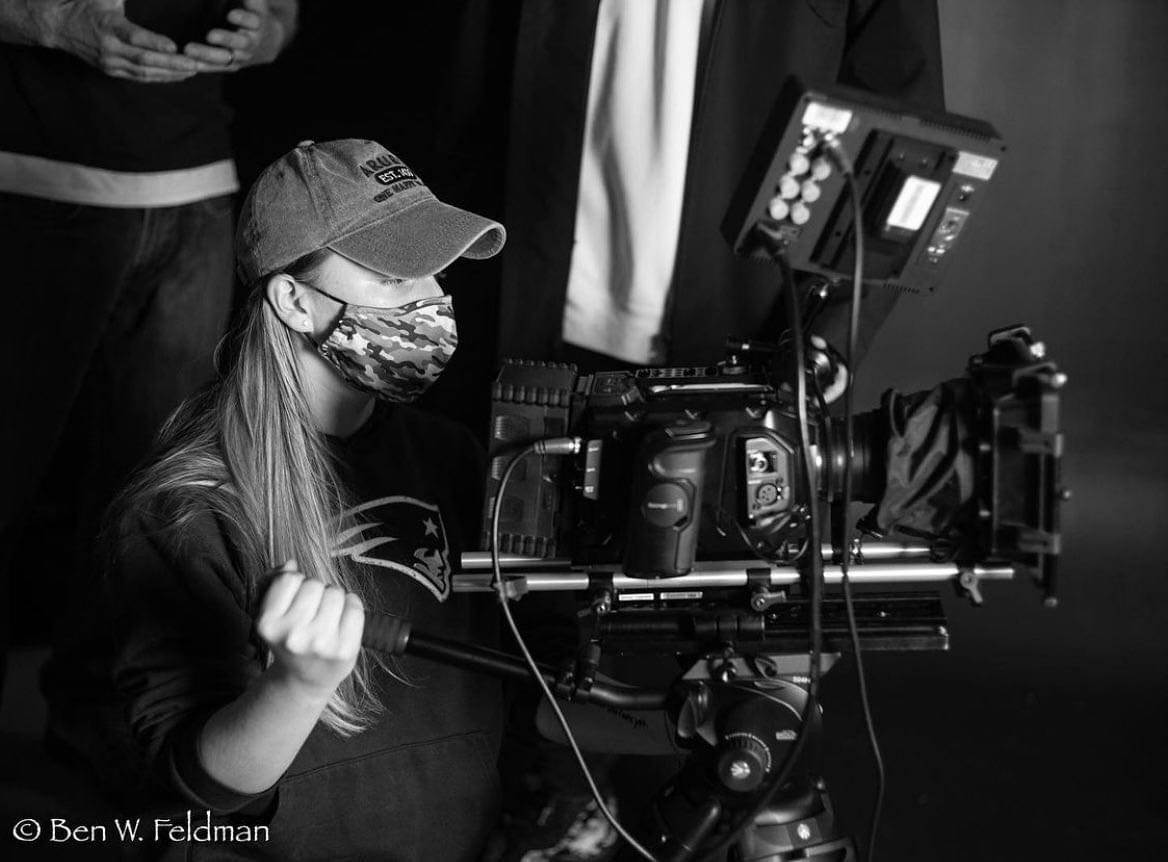 Gina Foley with a mask, black and white photo, working a professional video camera