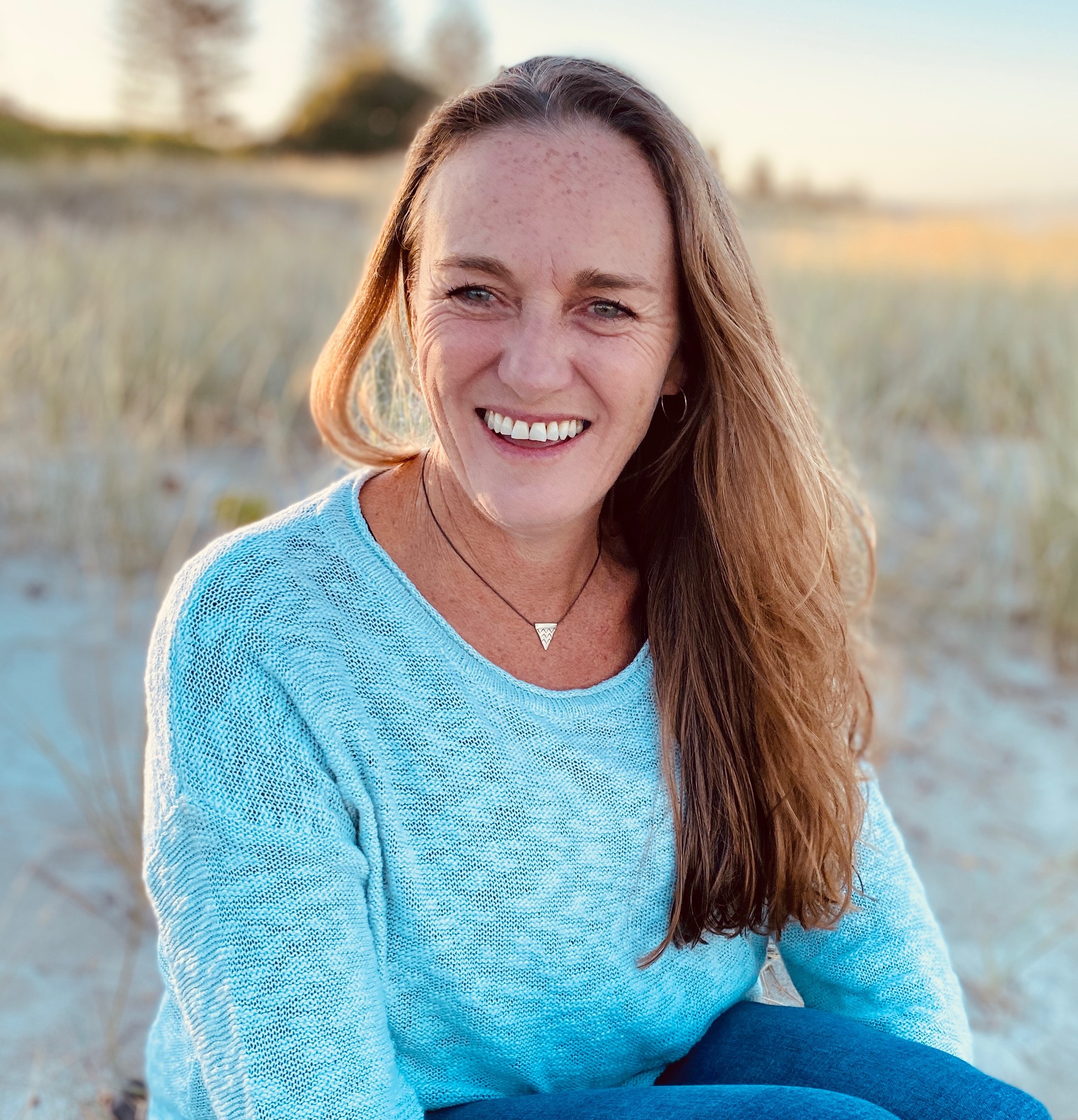 Headshot of Jodi Rodgers sitting on a beach wearing a blue top