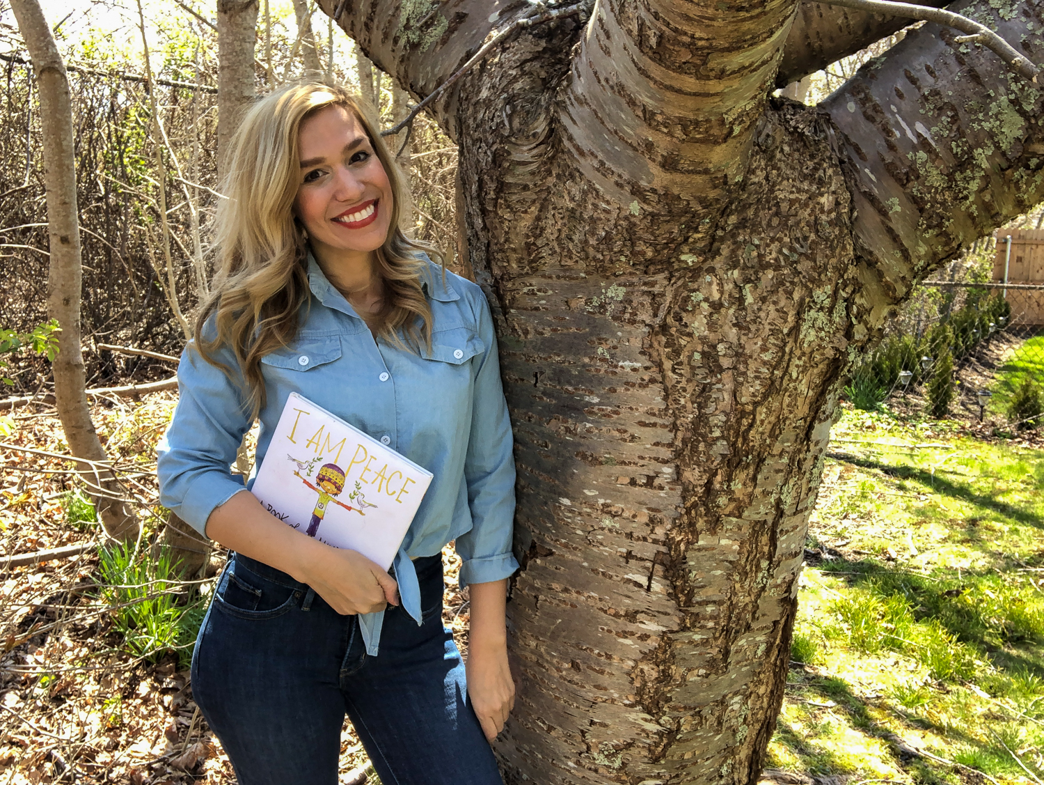 Katelyn Twardzik holding a children's book and leaning against a tree.