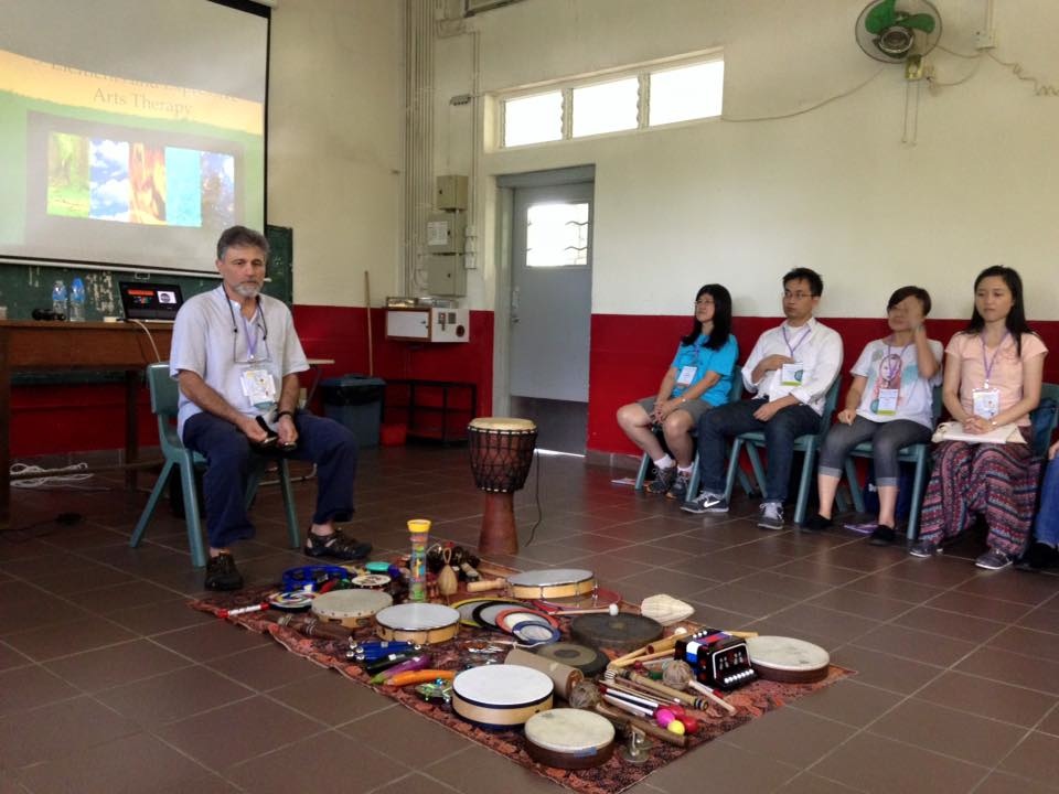 Kossak sits in a classroom in Hong Kong with drums and students.