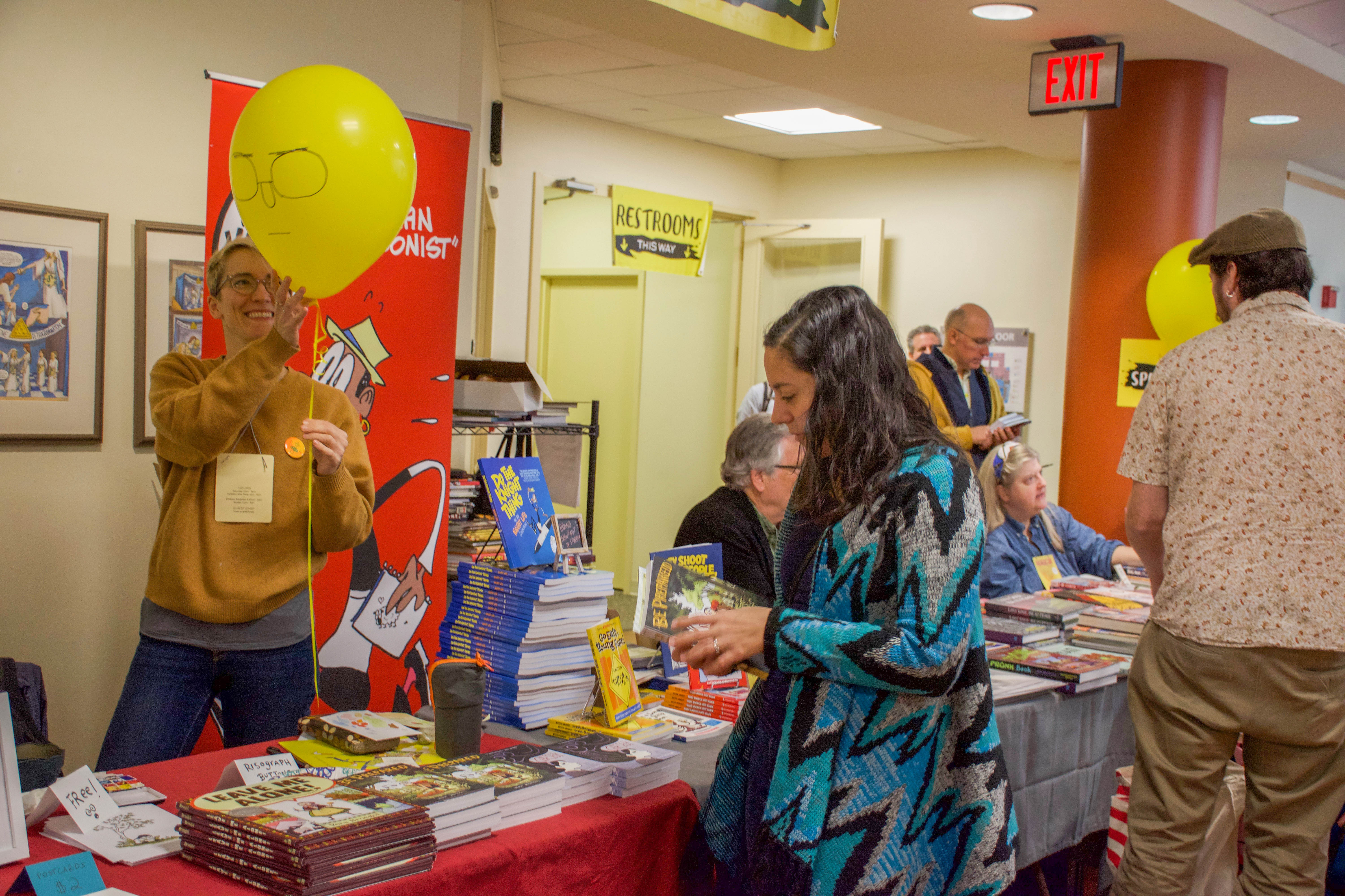 A woman plays with a yellow balloon at a table of comic books