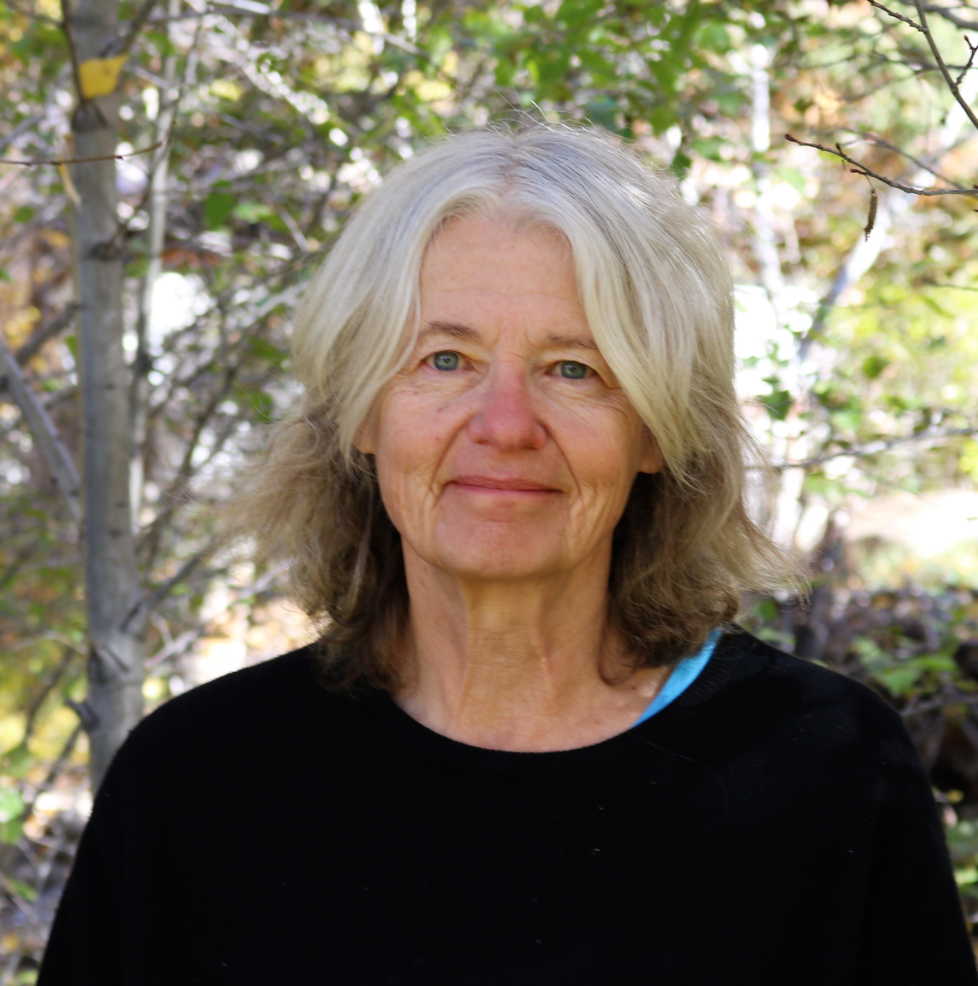 head shot of Melissa Kwasny posed in the foreground of a leafy tree