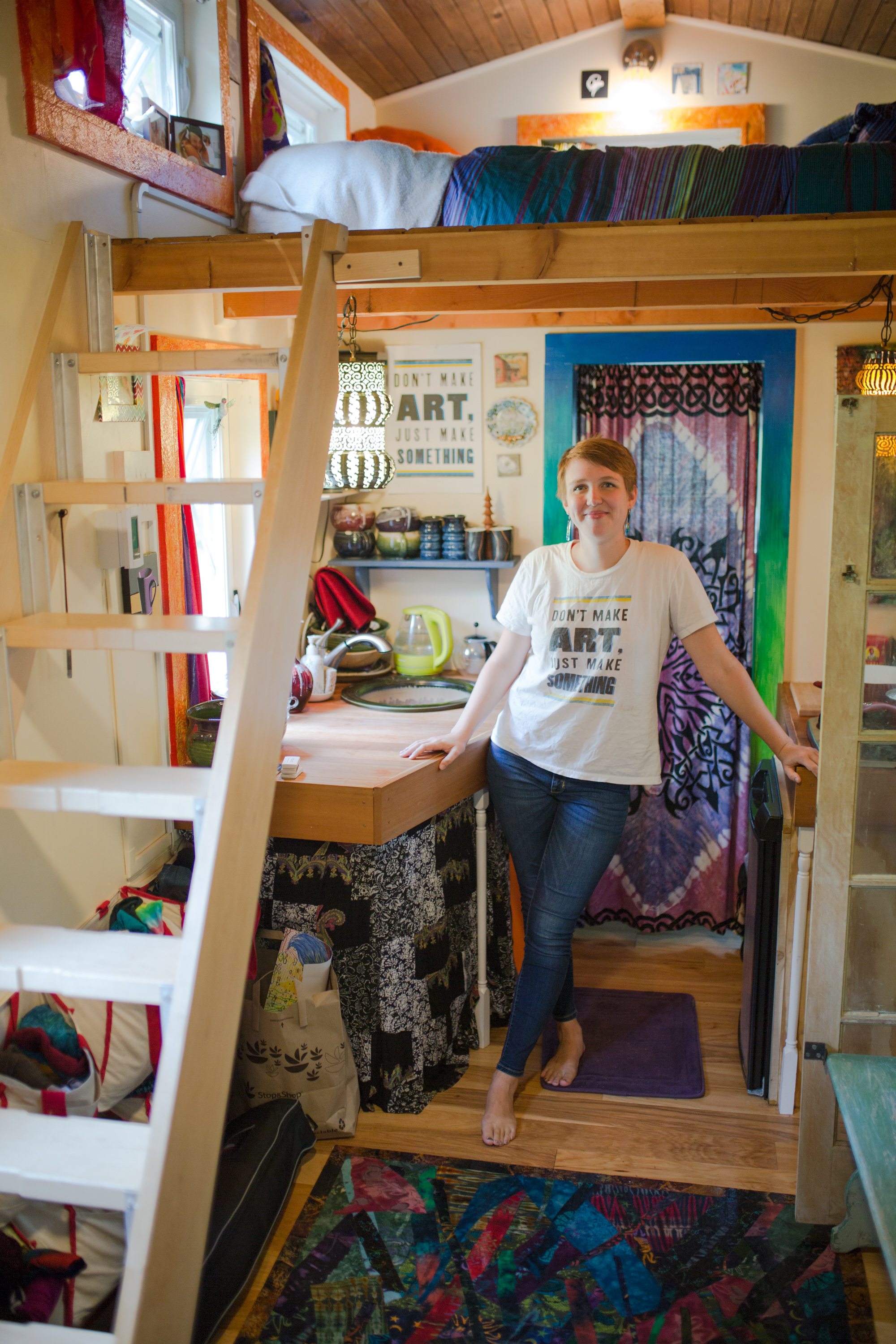 Miranda Aisling stands in the kitchen of her tiny house. Above her is her loft bedroom.