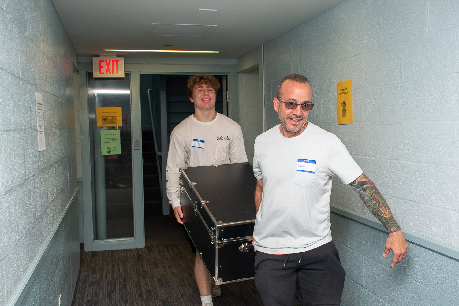 Father and son carry a trunk through a dorm hallway