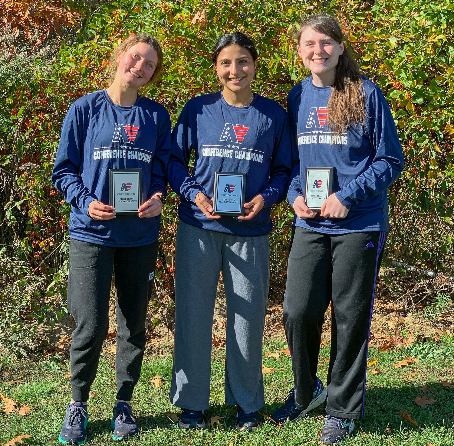 Three female cross country runners holding individual trophies
