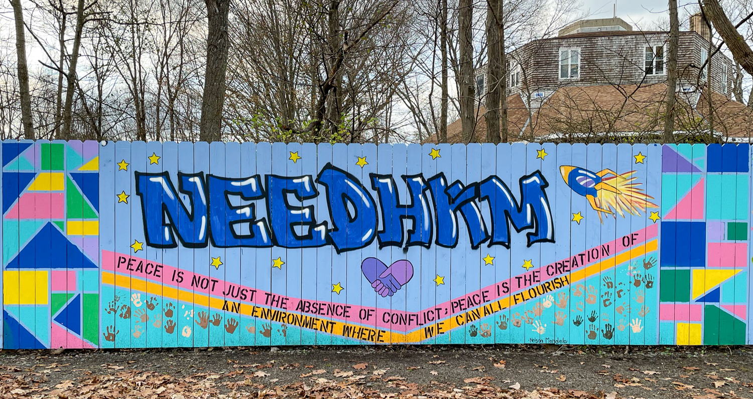 Panel of mural on a fence that reads "Needham"