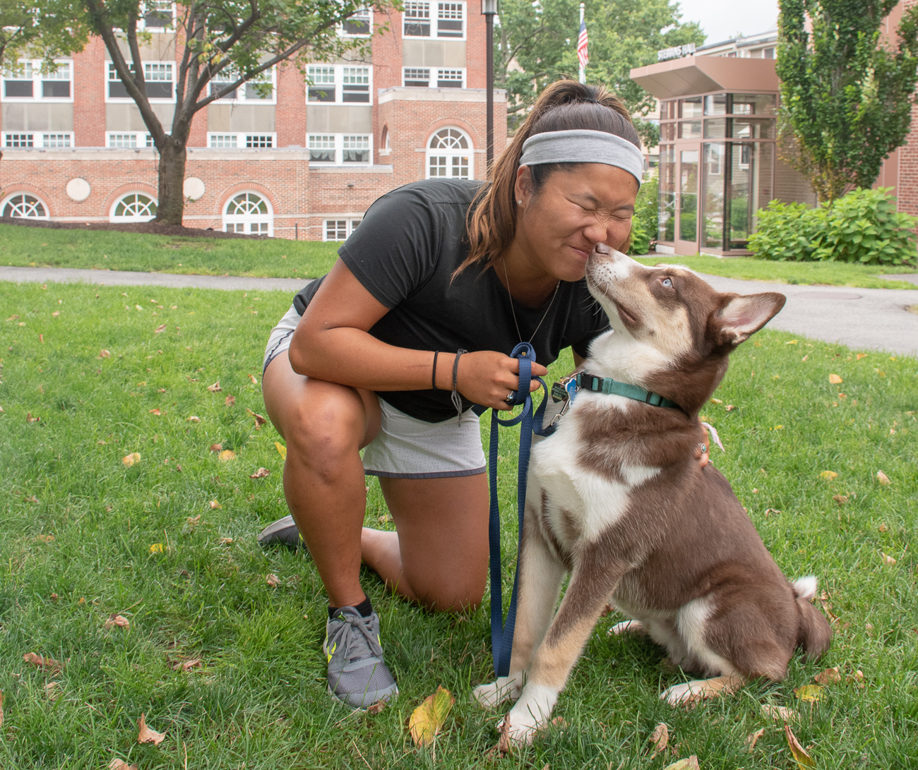 Theresa Pereira is bent down to eye level with the dog and has her face scrunched up as he noses her mouth.