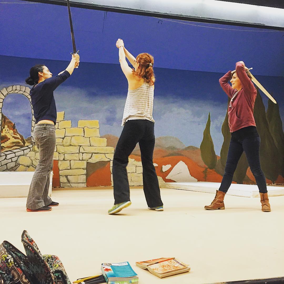 Three women on stage rehearsing a sword fight