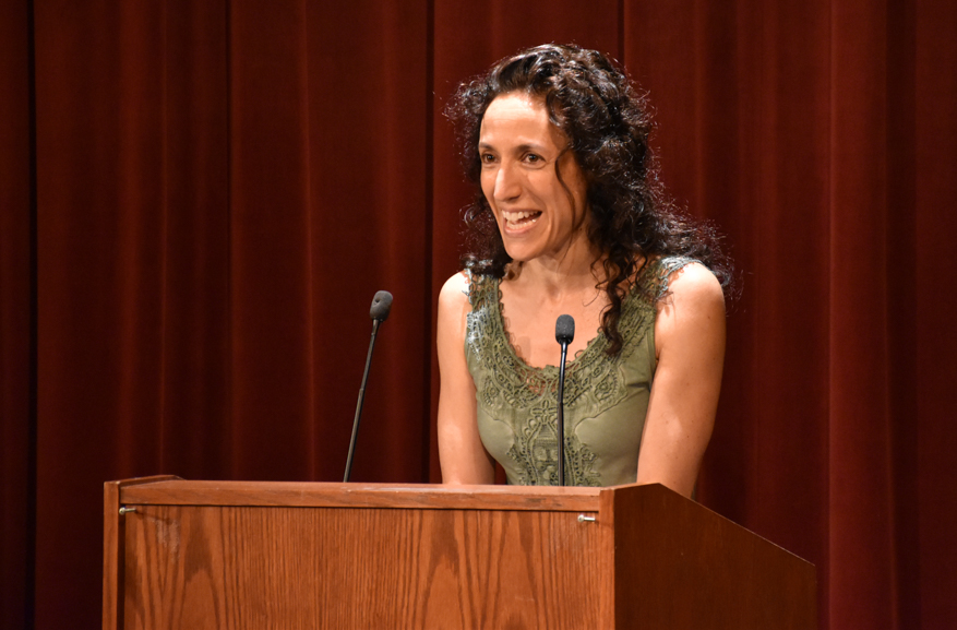 A smiling Rachel Kadish reads at a podium on the stage.