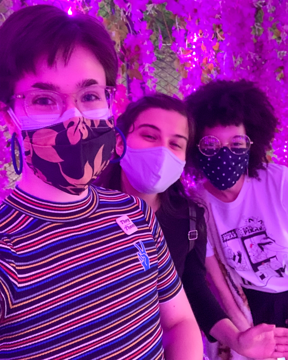 Three people wearing masks, pink light