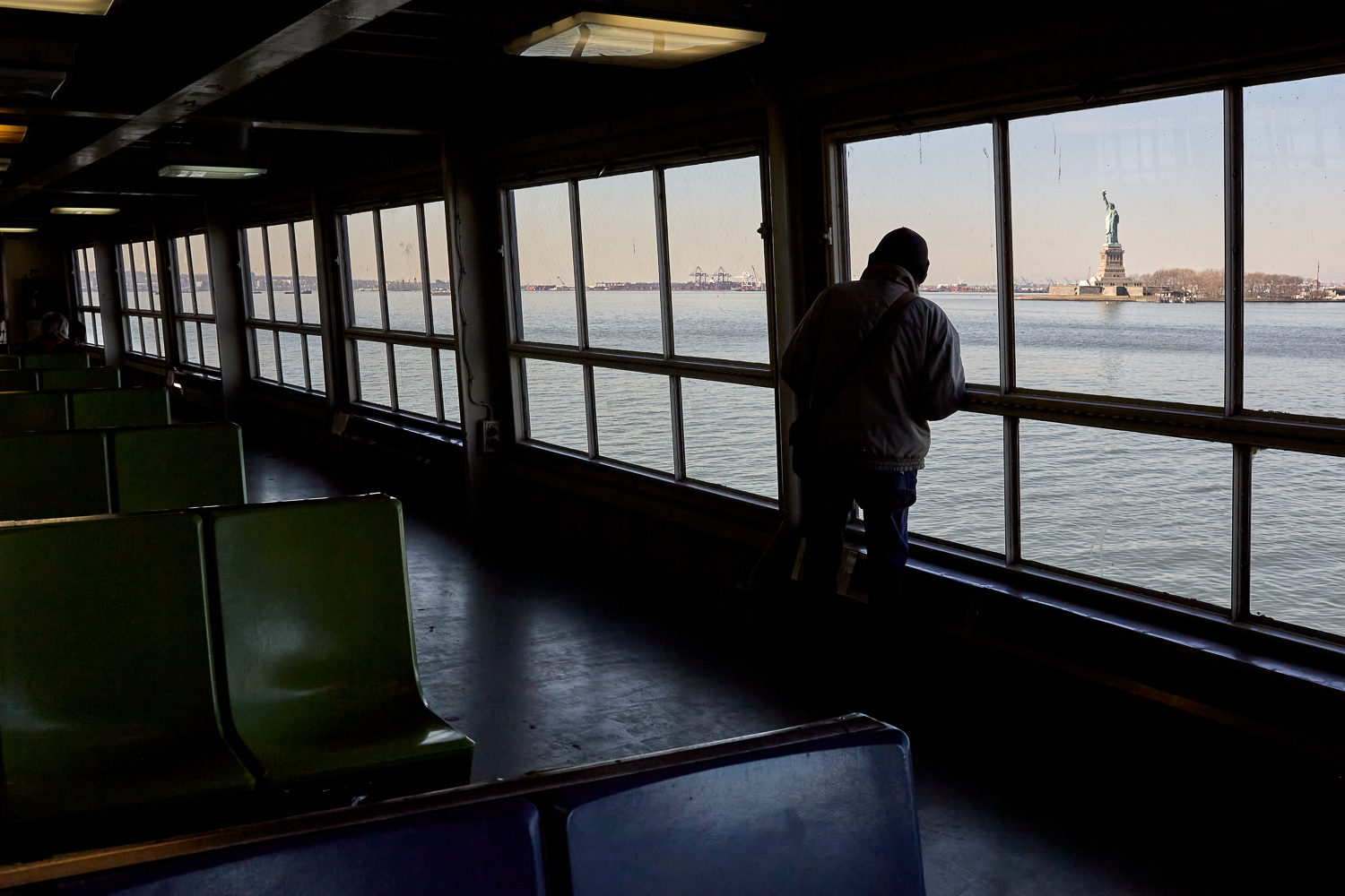 Someone looks out of the window of the Staten Island Ferry. Appears to be early evening.