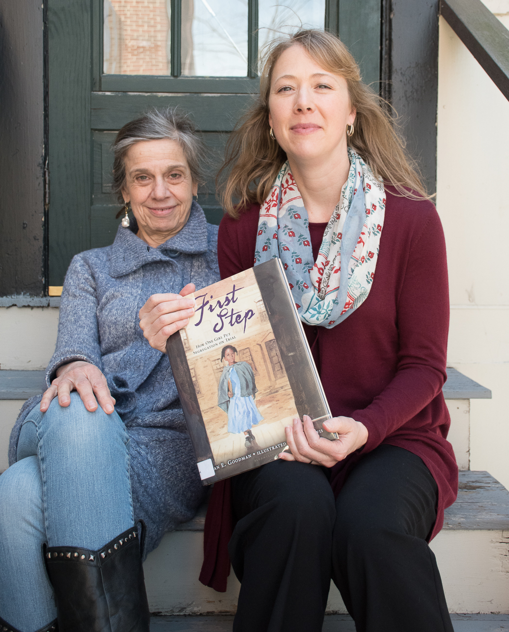Susan Goodman and Erika Dawes sit on steps outside holding a copy of one of Susan's books