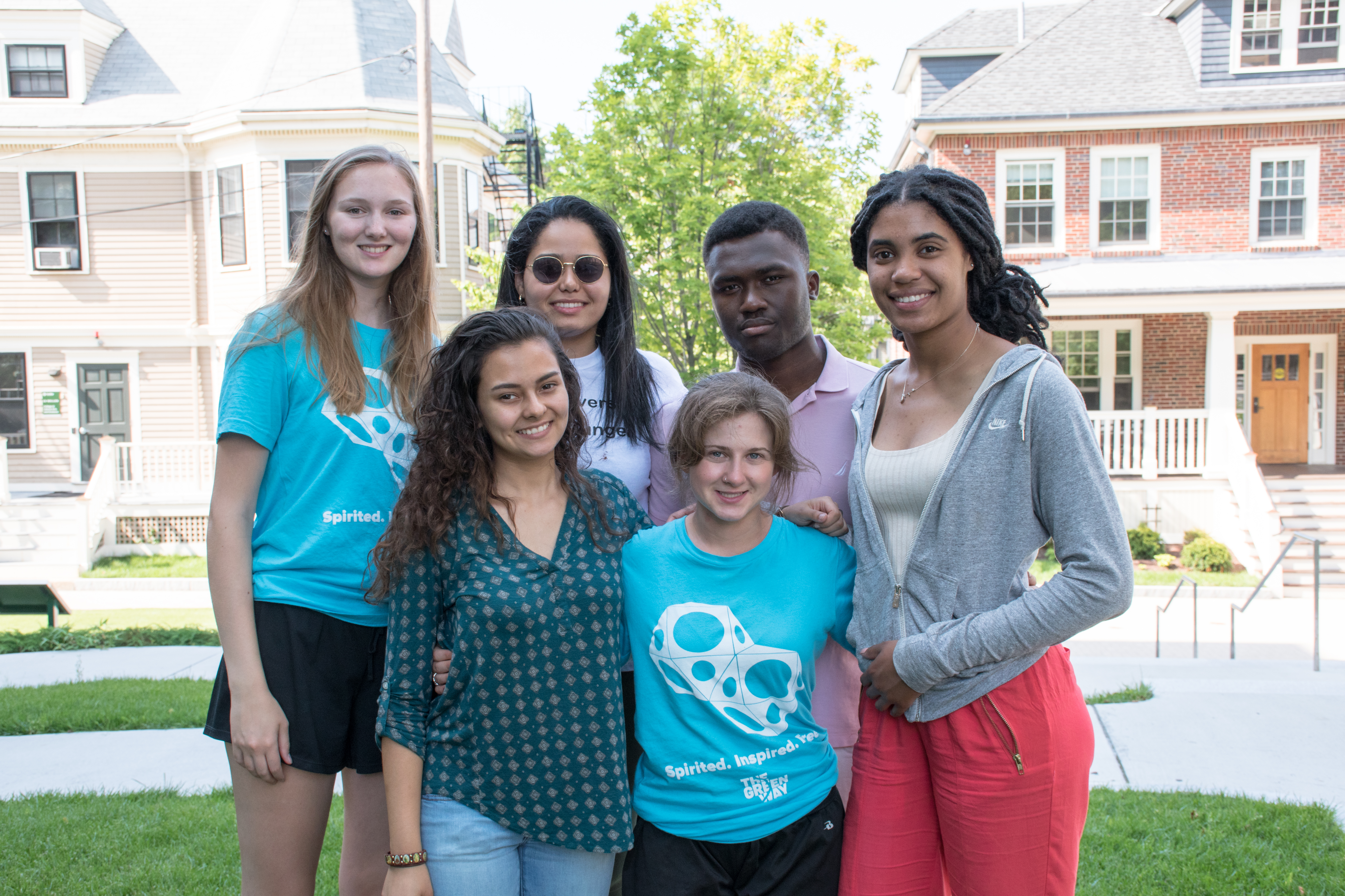 Seven students stand in a group picture on Doble Quad with two Victorian houses behind them.