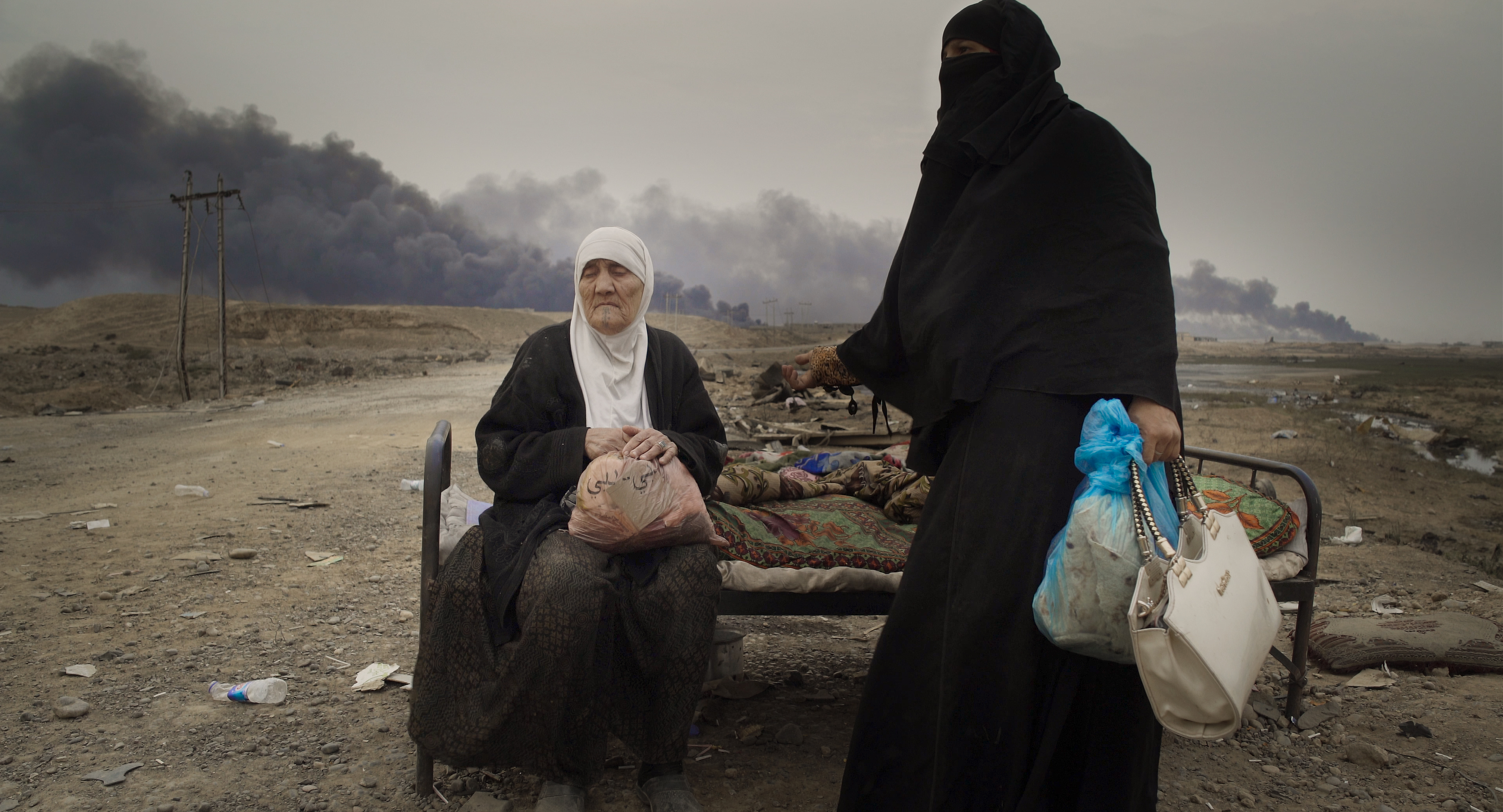 an older woman sits on an abandonded bed in the middle of the desert