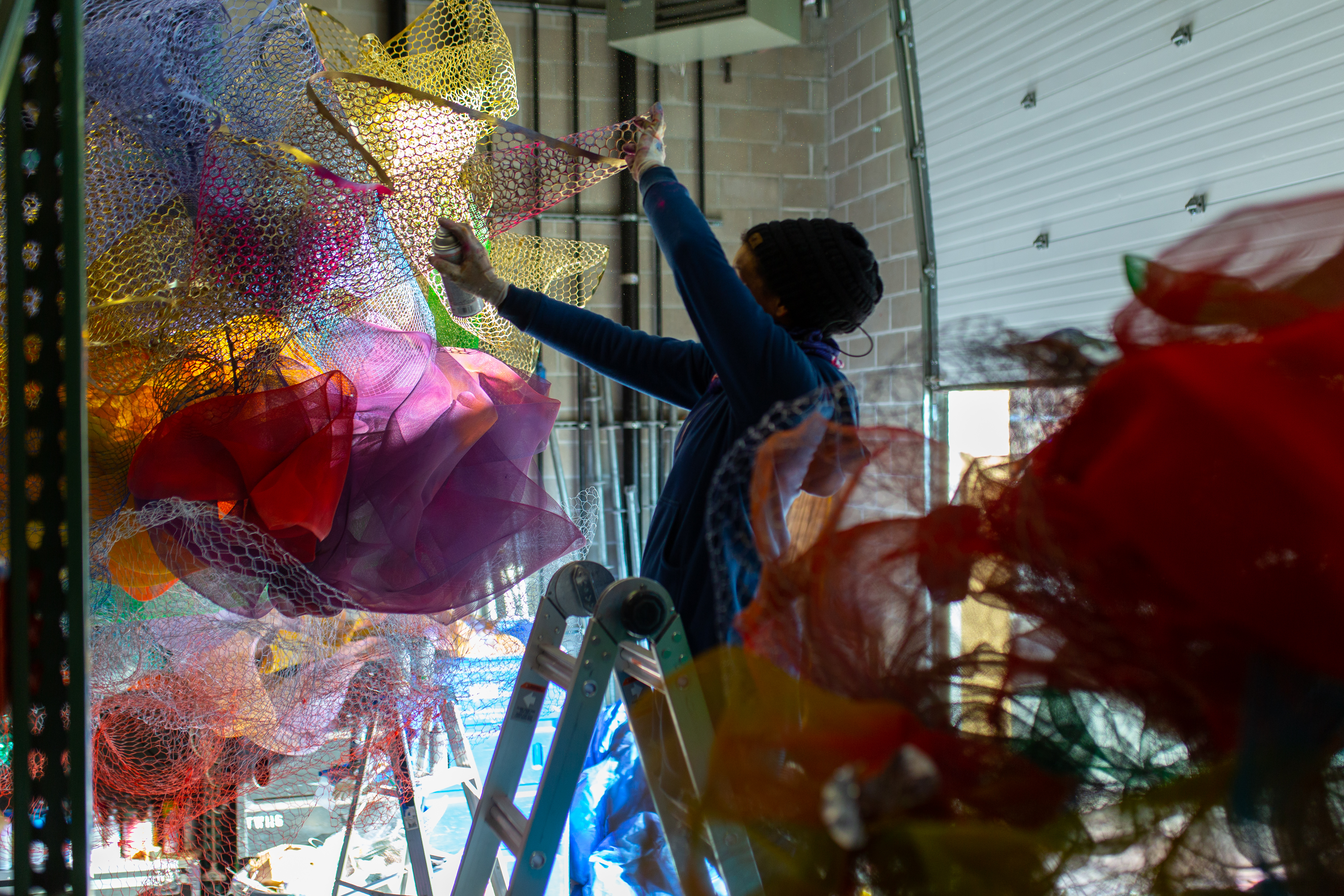 Cicely Carew in her studio standing on a ladder spray painting mesh.