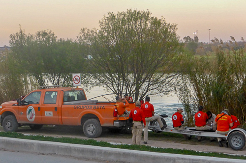 Mexican men in a orange clothes sit on a trailer behind an orange truck on the edge of a river
