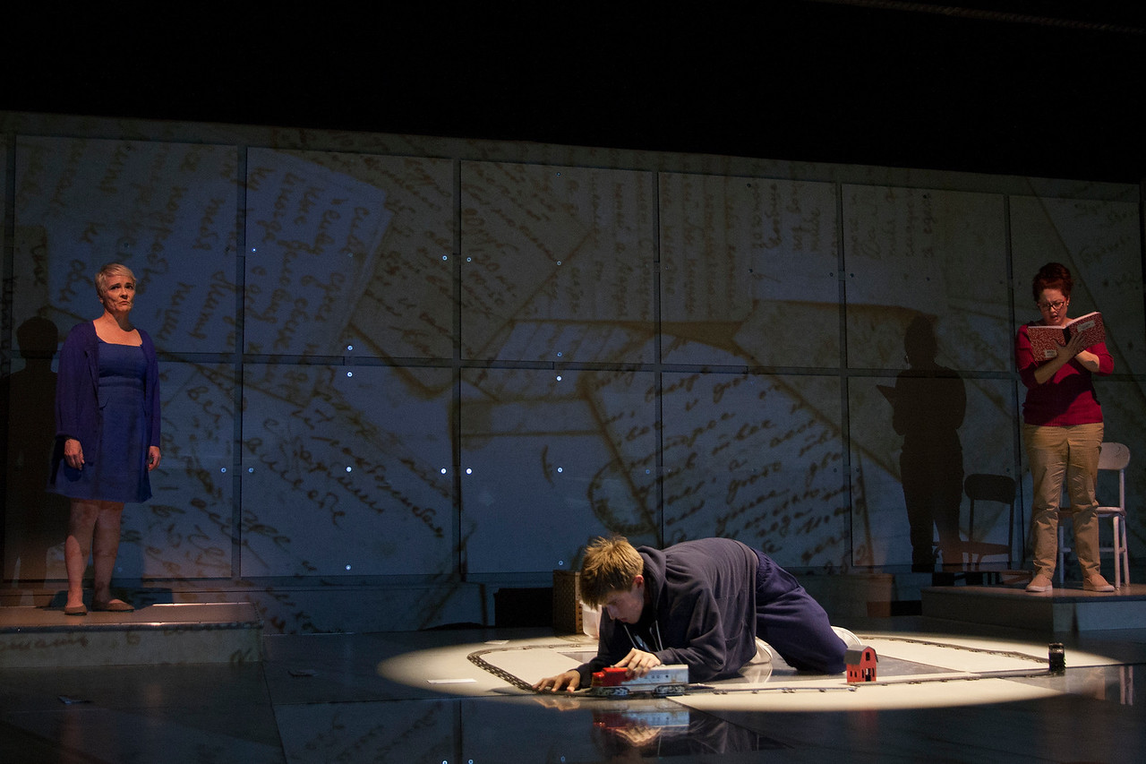 Three actors on stage during a performance with lights in a circle and a grid in the background