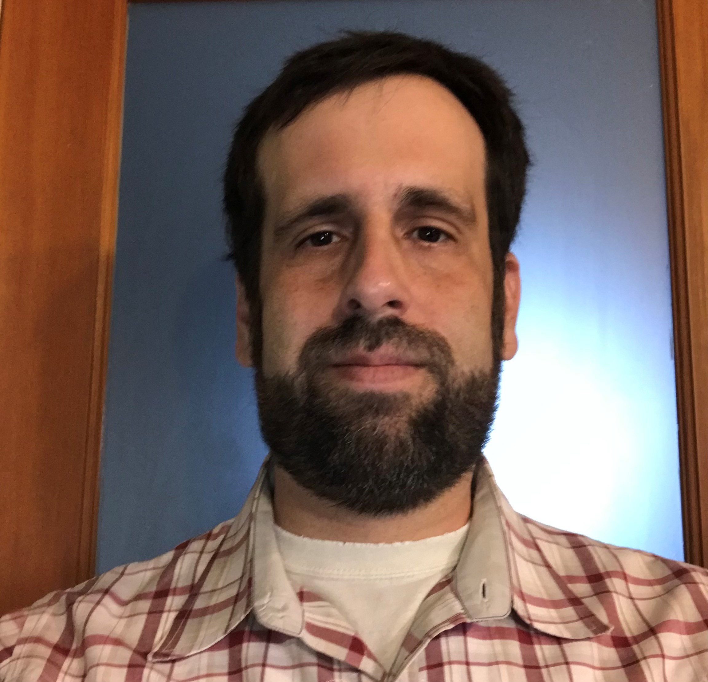 Headshot of Edward Yates. Edward has short brown hair and a beard. He wears a plaid flannel.