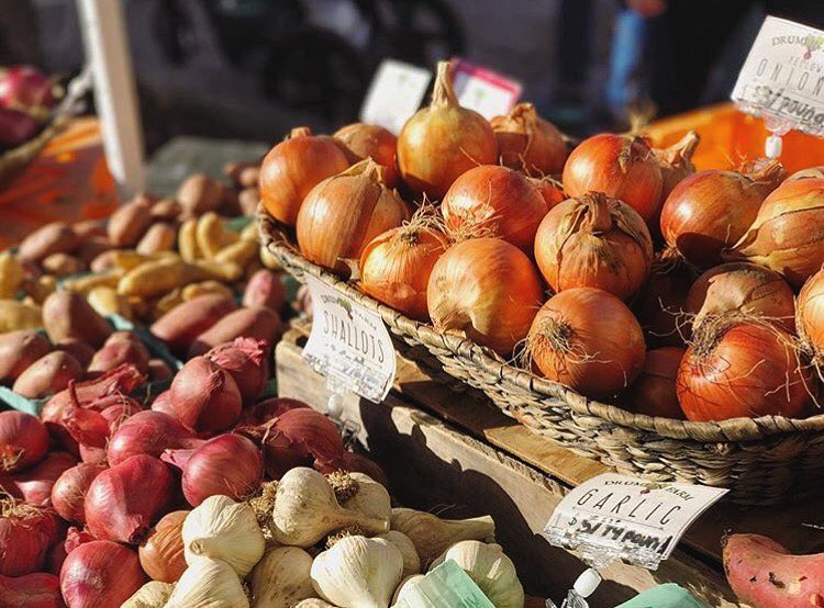 Closeup of onions, garlic, and shallots at an outdoor farmers' market