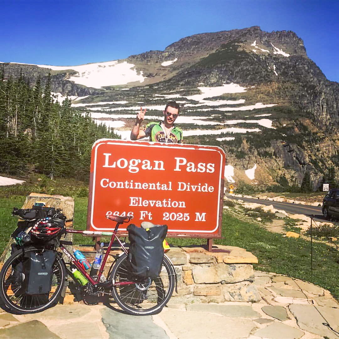 Brendan Walsh arrives at the Continental Divide. Poses in front of the continental divide sign announcing elevation at 2025 meters.