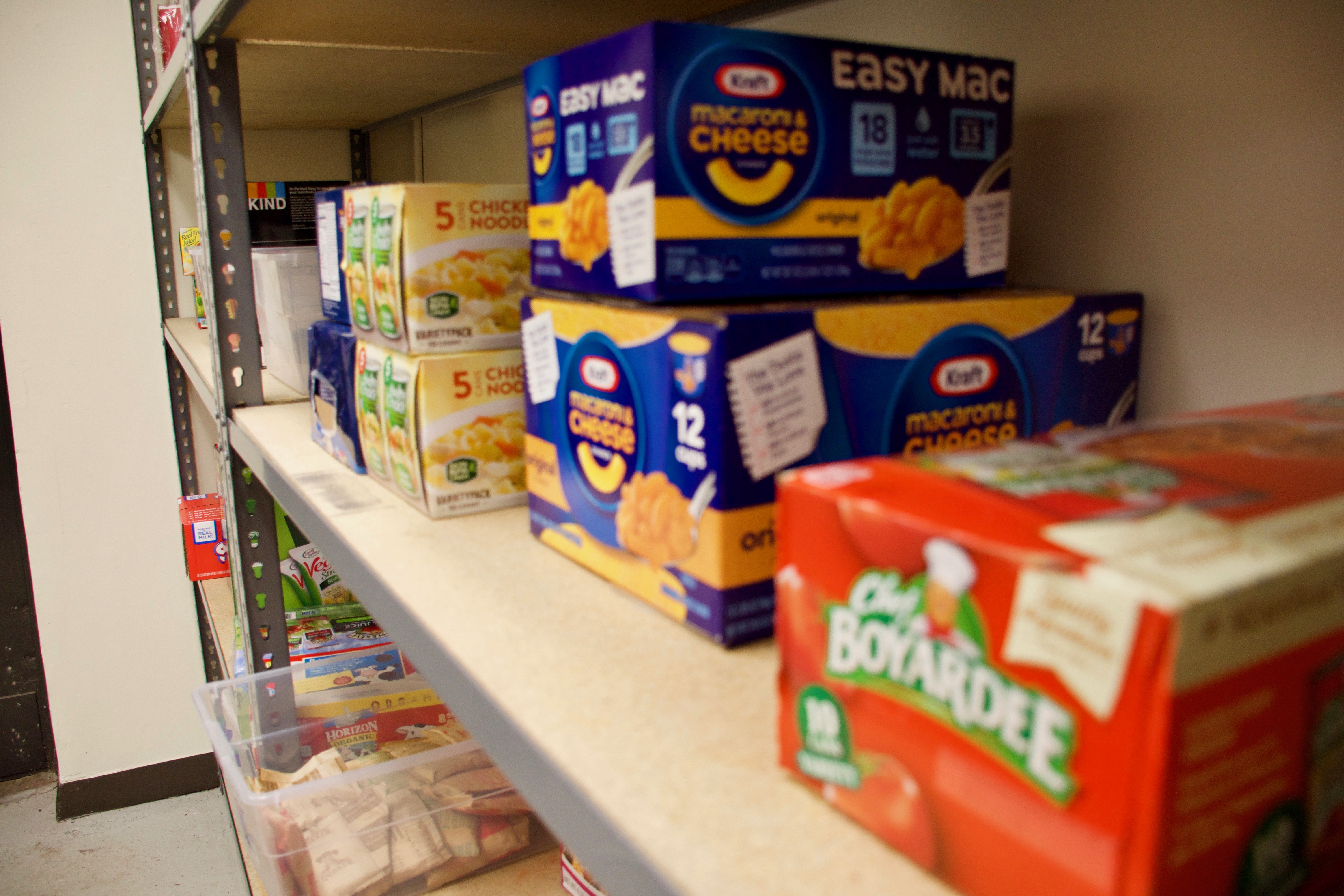 A set of shelves with macaroni and cheese and noodles stacked up on top of one another in a food pantry.