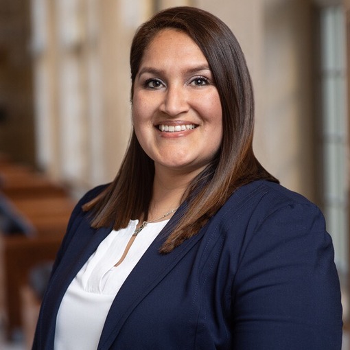 Professional photo of a woman with wearing a blazer smiling and standing in a school building.