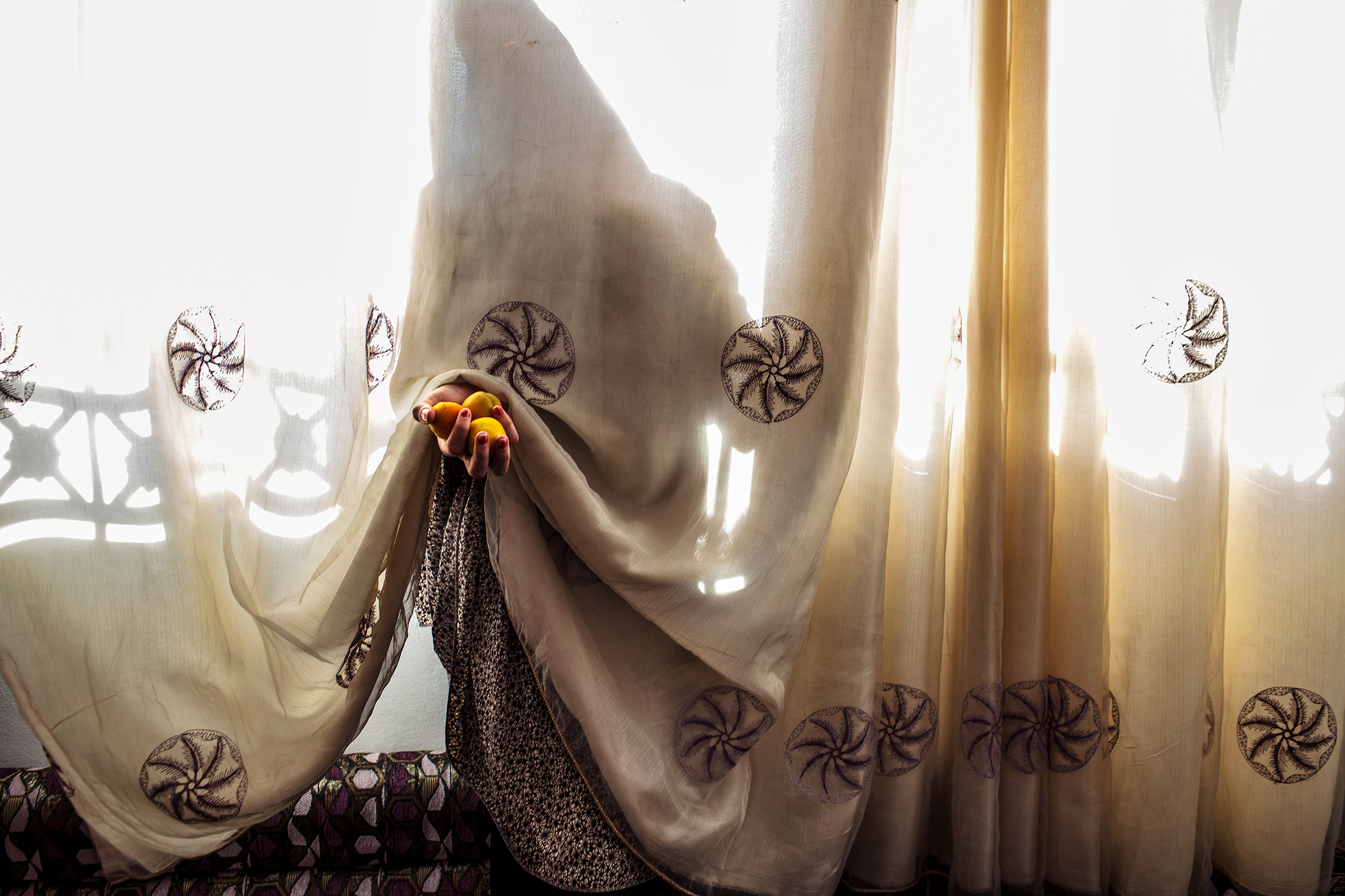 a person stands behind a lace curtain holding out a handful of orange fruit