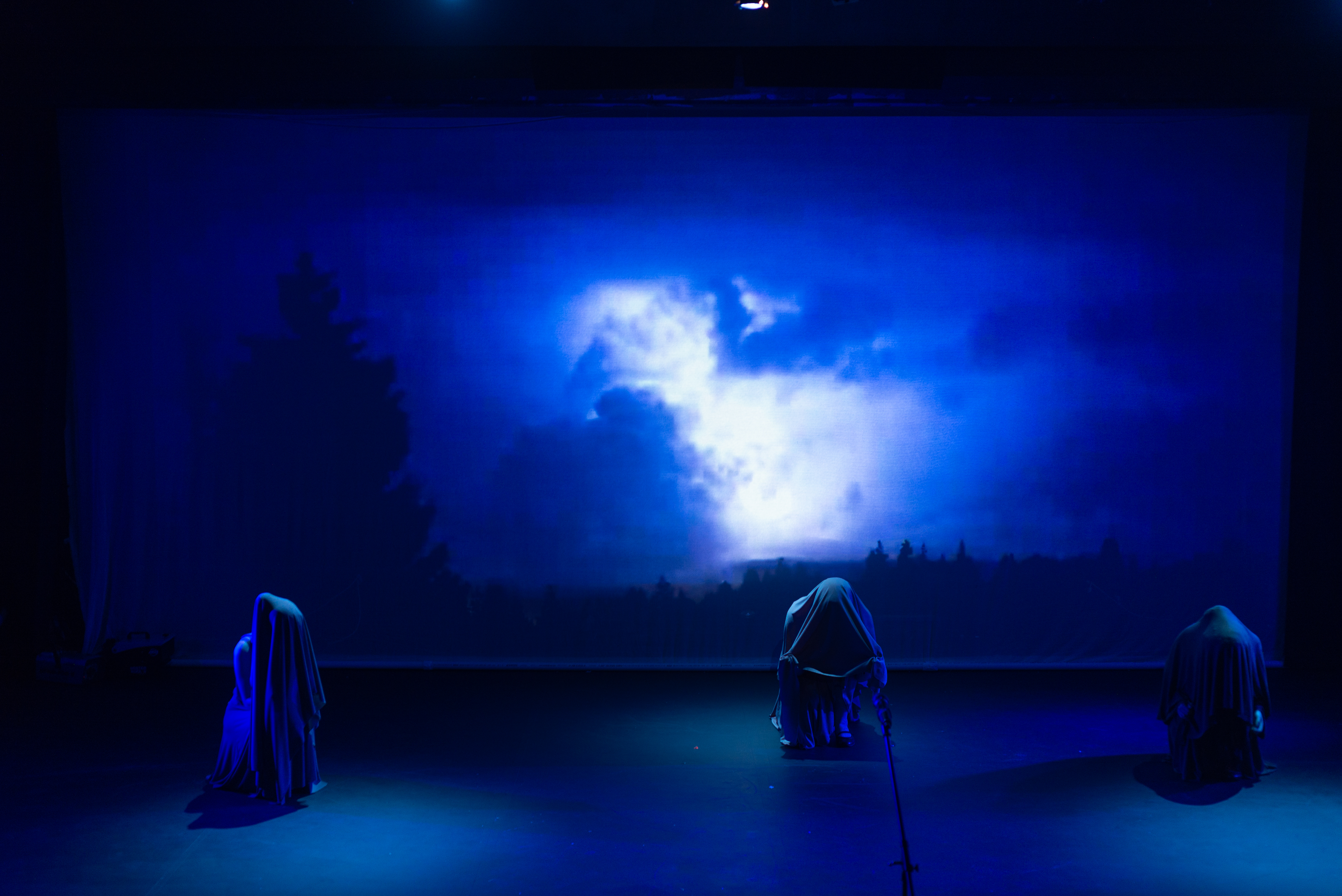 A photograph of the Marran Theater stage during a dress rehearsal of the Oxford Street Players porduction of Macbeth with three witches in front of a screen of blue clouds