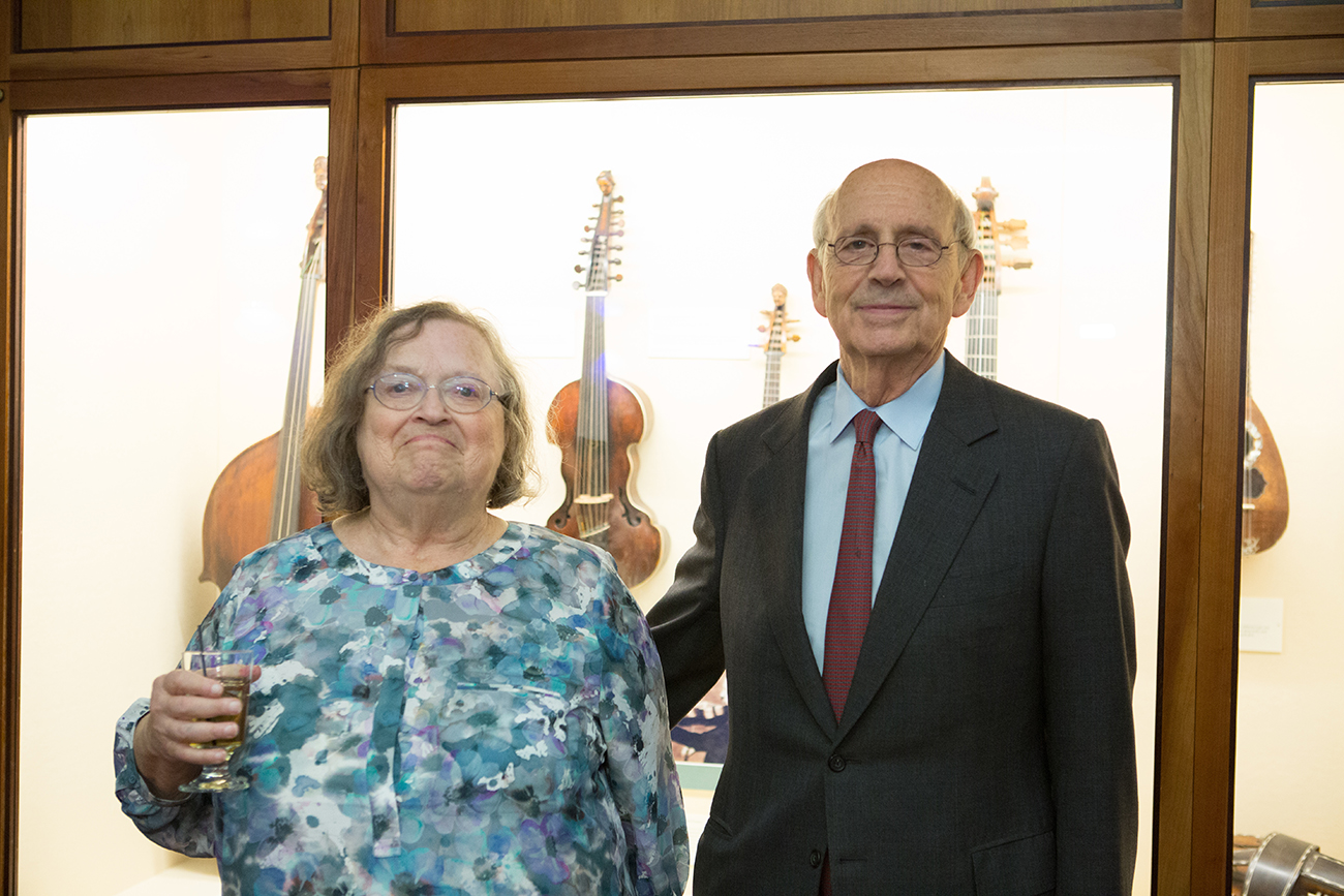 Man and a woman holding a drink and posing for a photo and smiling in front of a case of instruments.
