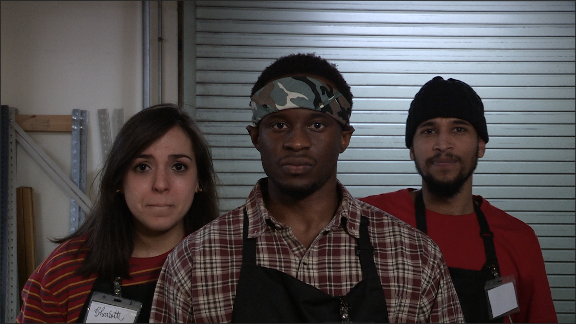 Three people wearing black aprons look into the camera 