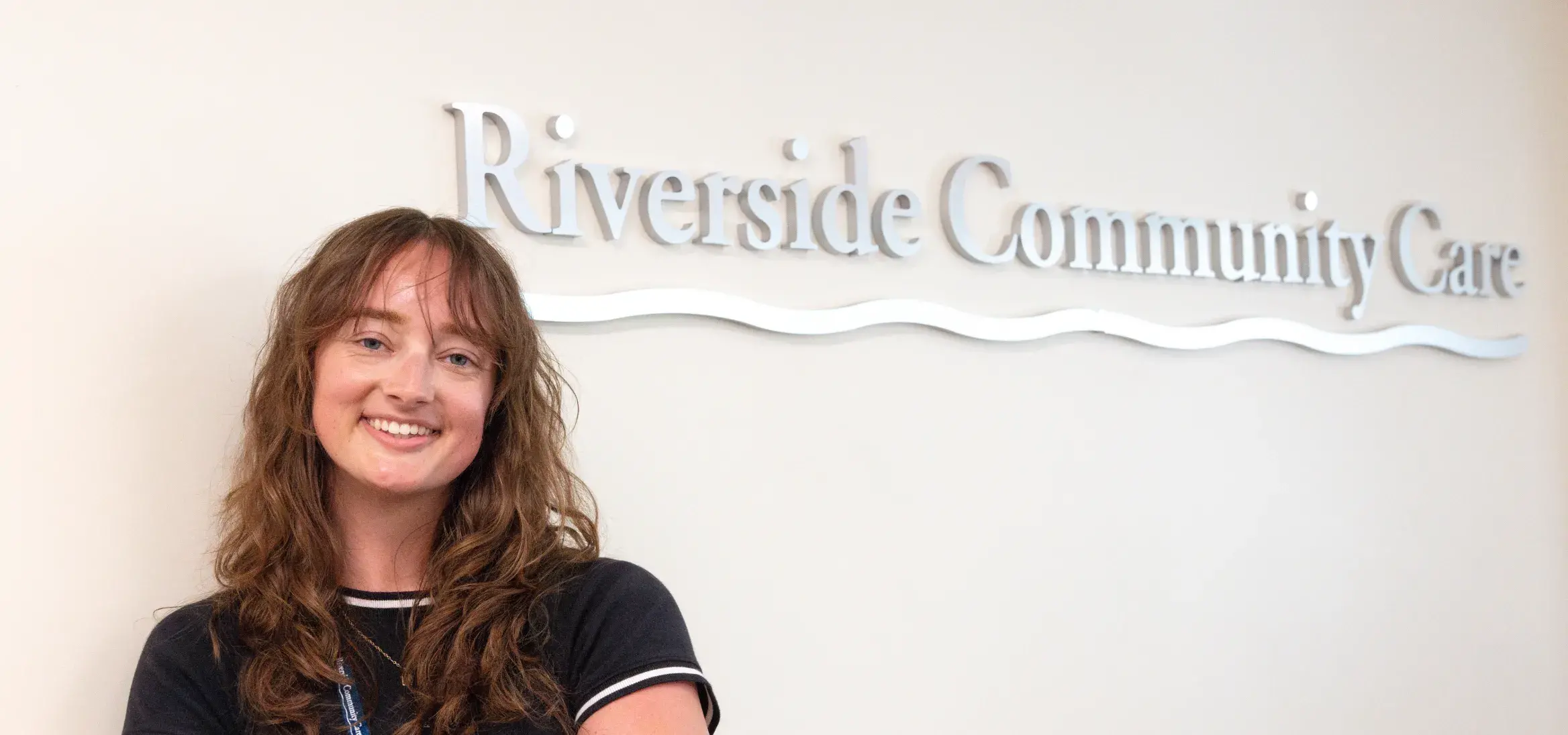 Student standing in front of Riverside Community Care sign against a white wall