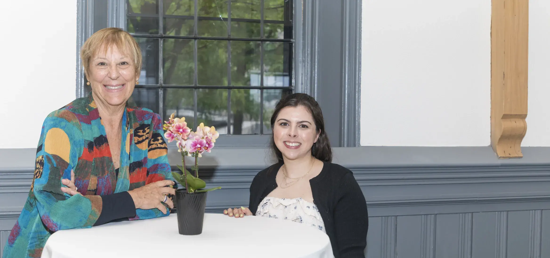 two women standing in front of round white table with flowers