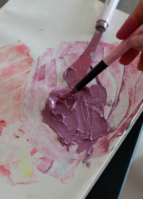 Hand holding a paintbrush, painting with pink and purple paint on a piece of paper.