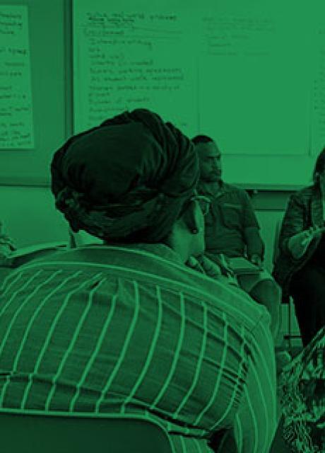 Photo shaded green of teachers sitting in a circle listening to instructor
