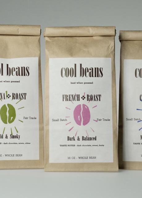 three bags of coffee grounds in brown bags with "Cool Beans" white label on them.