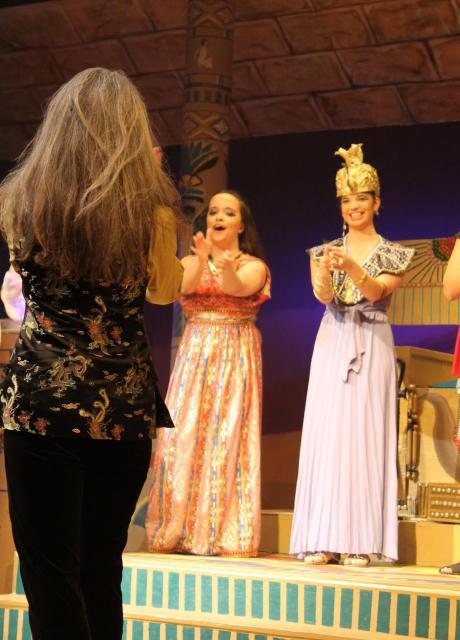 student actors in dresses and professor clapping on stage at the end of a play