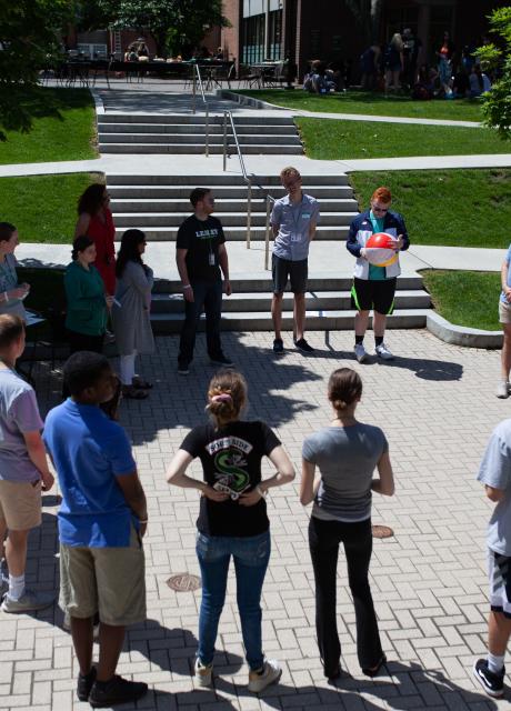 Students standing outside on the quad in a circle on a sunny summer day
